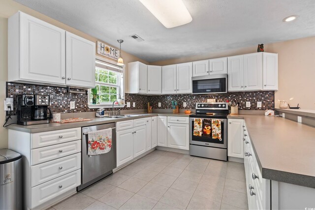 kitchen with hanging light fixtures, backsplash, stainless steel appliances, white cabinetry, and sink