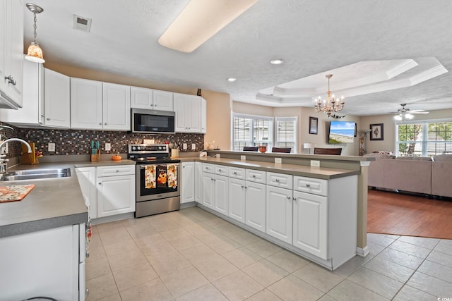 kitchen featuring light wood-type flooring, a raised ceiling, ceiling fan with notable chandelier, decorative light fixtures, and appliances with stainless steel finishes