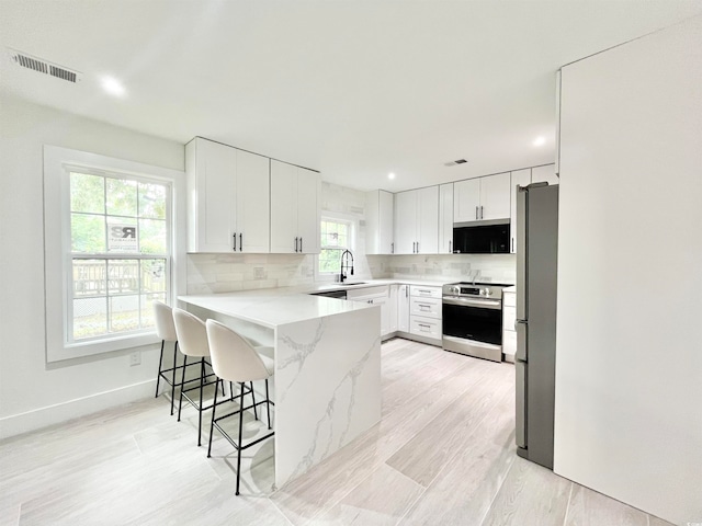 kitchen with a breakfast bar area, backsplash, appliances with stainless steel finishes, light hardwood / wood-style floors, and white cabinets