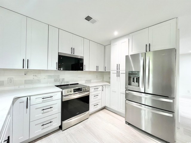 kitchen with light wood-type flooring, appliances with stainless steel finishes, white cabinetry, and decorative backsplash