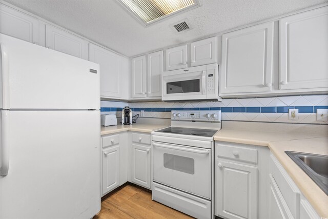 kitchen with white appliances, light hardwood / wood-style flooring, white cabinets, and decorative backsplash