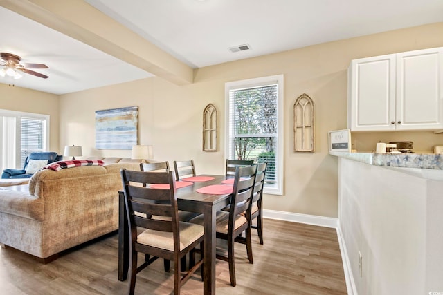 dining space featuring ceiling fan, wood-type flooring, and beam ceiling