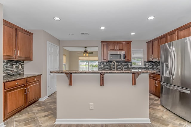 kitchen featuring stainless steel appliances, a center island with sink, a wealth of natural light, and a breakfast bar area