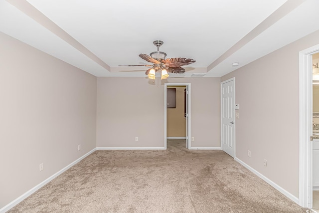 carpeted spare room with a tray ceiling and ceiling fan