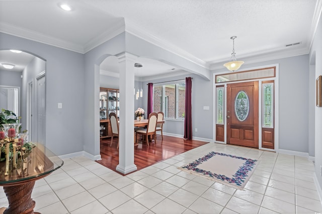 entryway with light wood-type flooring, a textured ceiling, crown molding, and ornate columns