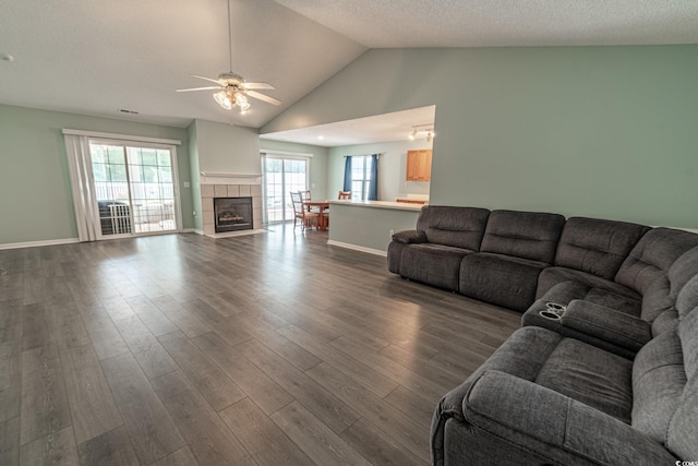 living room with a textured ceiling, dark hardwood / wood-style floors, a tile fireplace, lofted ceiling, and ceiling fan