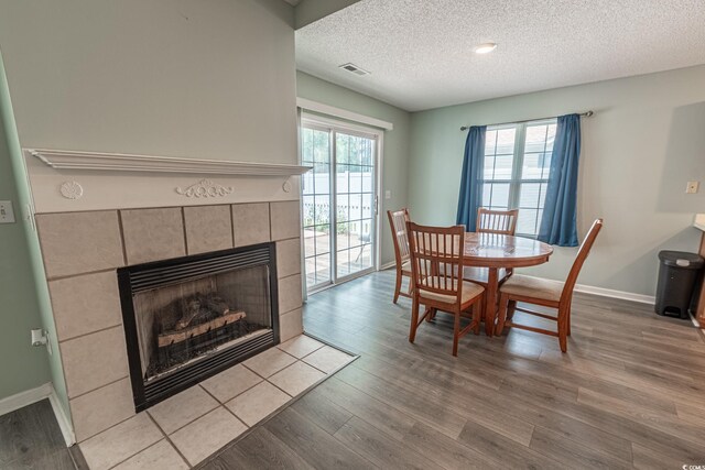 dining area featuring a textured ceiling, light hardwood / wood-style flooring, and a tiled fireplace