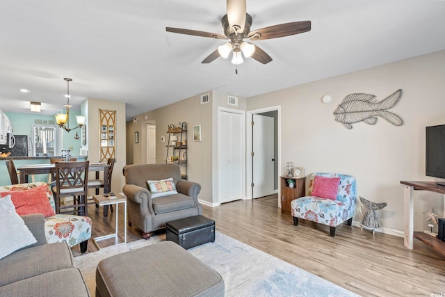 living room featuring ceiling fan with notable chandelier and light hardwood / wood-style floors