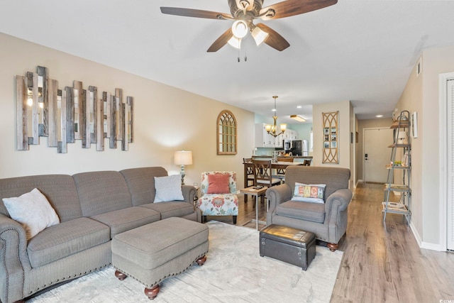 living area with ceiling fan with notable chandelier, baseboards, and wood finished floors