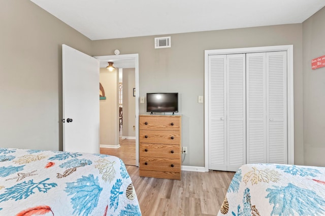 bedroom with a closet, light wood-type flooring, visible vents, and baseboards