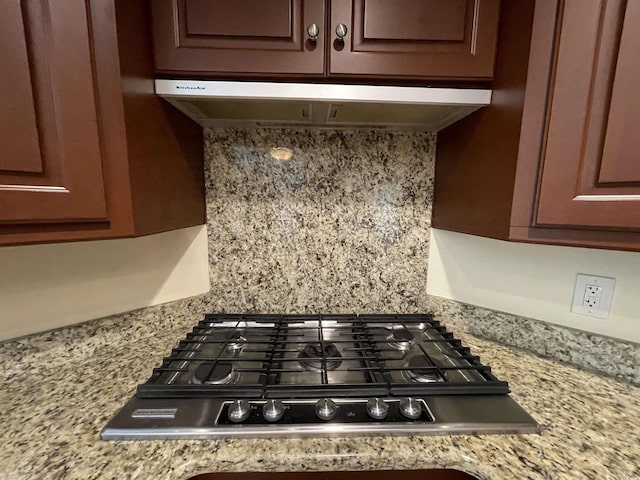 interior details featuring light stone countertops, backsplash, and stainless steel gas stovetop