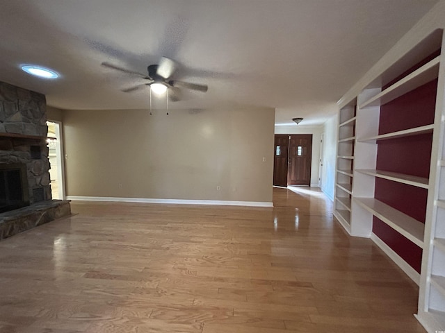 unfurnished living room featuring built in features, a fireplace, light hardwood / wood-style floors, and ceiling fan