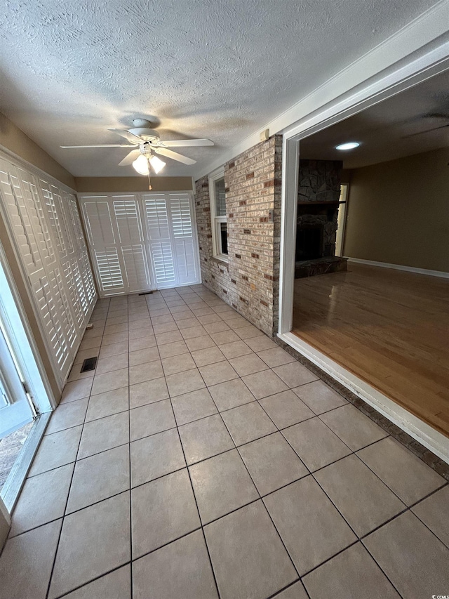 interior space with light tile patterned flooring, a textured ceiling, ceiling fan, and a fireplace