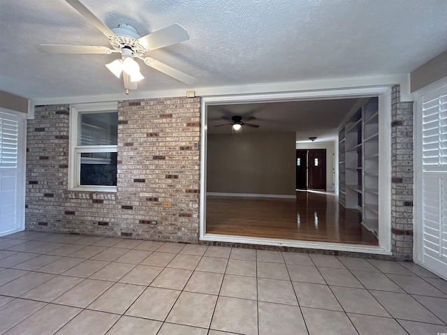 tiled spare room with ceiling fan, built in shelves, a textured ceiling, and brick wall