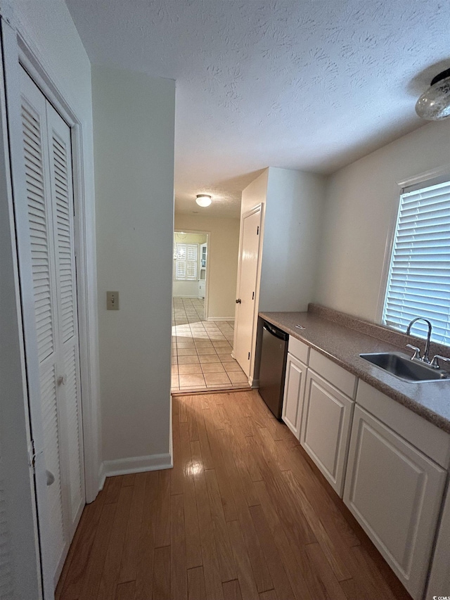 kitchen featuring sink, light hardwood / wood-style flooring, dishwasher, white cabinetry, and a textured ceiling