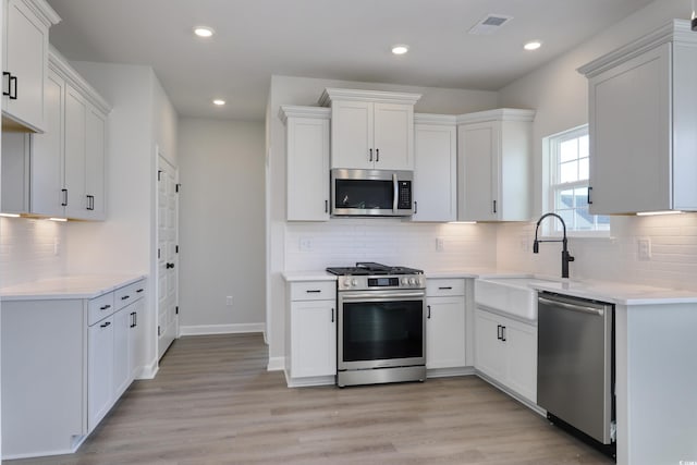 kitchen with sink, light hardwood / wood-style flooring, decorative backsplash, white cabinets, and appliances with stainless steel finishes