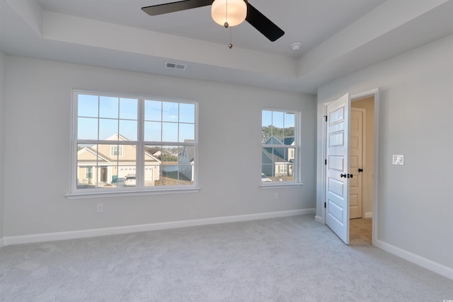 carpeted empty room with ceiling fan and a raised ceiling