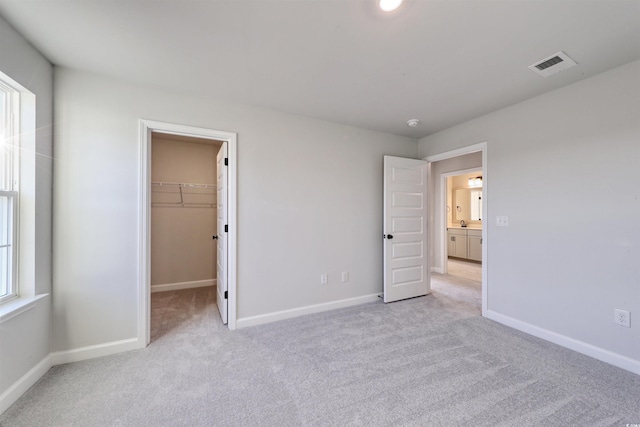 unfurnished bedroom with light carpet, a walk in closet, and a closet