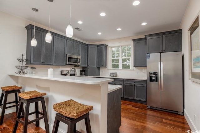 kitchen with appliances with stainless steel finishes, a breakfast bar, dark wood-type flooring, a peninsula, and light countertops