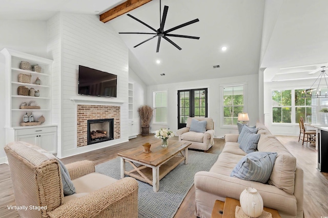 living room featuring a fireplace, beam ceiling, high vaulted ceiling, light hardwood / wood-style flooring, and ceiling fan with notable chandelier