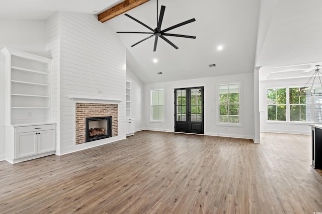 unfurnished living room featuring light hardwood / wood-style floors, beamed ceiling, high vaulted ceiling, a fireplace, and french doors