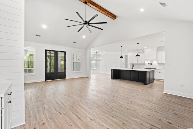 unfurnished living room featuring ceiling fan with notable chandelier, beam ceiling, high vaulted ceiling, light hardwood / wood-style flooring, and french doors