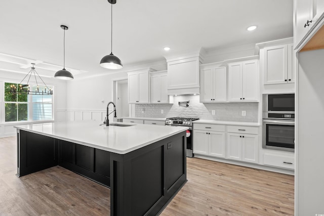 kitchen with stainless steel appliances, white cabinetry, decorative light fixtures, an island with sink, and light hardwood / wood-style flooring