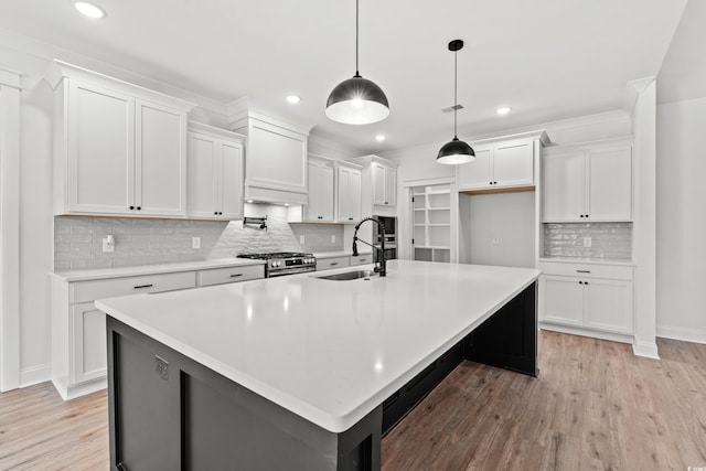 kitchen featuring sink, a large island with sink, tasteful backsplash, light hardwood / wood-style flooring, and white cabinets