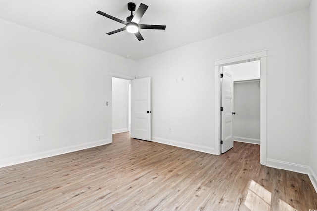 unfurnished bedroom featuring a closet, a spacious closet, ceiling fan, and light hardwood / wood-style flooring