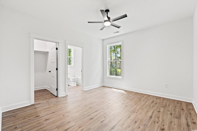 unfurnished bedroom with light wood-type flooring, a spacious closet, ceiling fan, and a closet