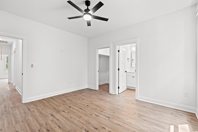 unfurnished bedroom featuring ensuite bath, ceiling fan, a spacious closet, a closet, and light wood-type flooring