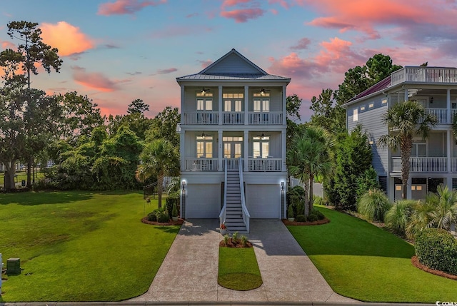 raised beach house with ceiling fan, stairs, a yard, a balcony, and an attached garage