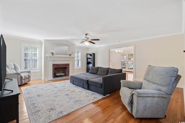 living room featuring light hardwood / wood-style flooring, ceiling fan with notable chandelier, a wealth of natural light, and a brick fireplace