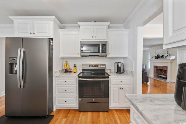 kitchen with light stone counters, stainless steel appliances, light hardwood / wood-style floors, and a brick fireplace