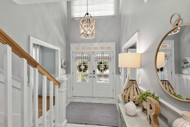 entryway featuring french doors, light wood-type flooring, a high ceiling, and a notable chandelier