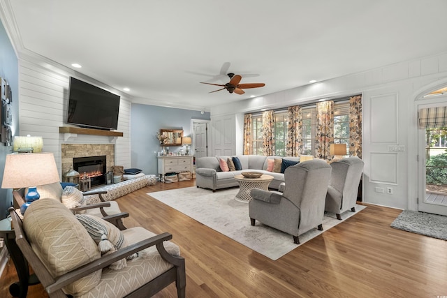 living room featuring hardwood / wood-style floors, a large fireplace, ceiling fan, and crown molding