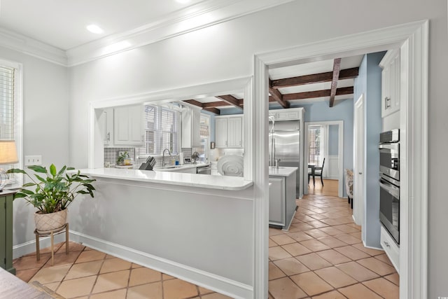 kitchen with beam ceiling, sink, light tile patterned floors, kitchen peninsula, and white cabinets