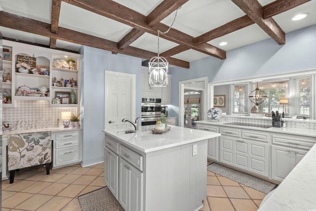 kitchen featuring tasteful backsplash, sink, pendant lighting, a notable chandelier, and an island with sink