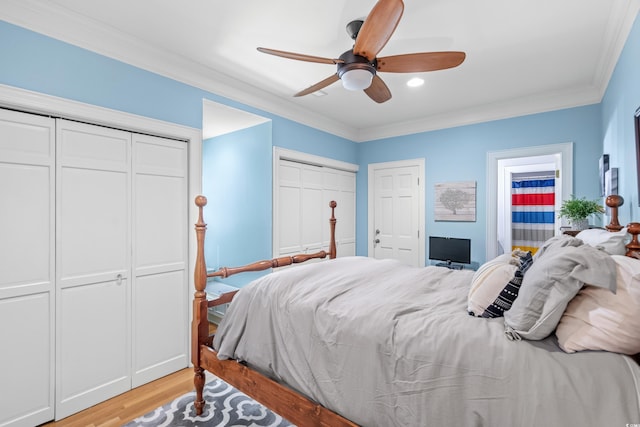 bedroom with ceiling fan, multiple closets, crown molding, and light hardwood / wood-style flooring