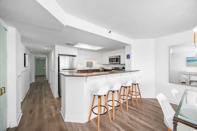 kitchen with appliances with stainless steel finishes, a breakfast bar, white cabinets, kitchen peninsula, and light hardwood / wood-style flooring