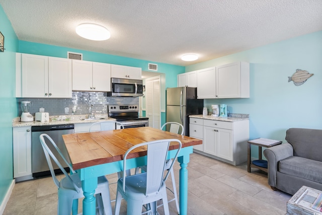 kitchen featuring a textured ceiling, stainless steel appliances, white cabinets, and tasteful backsplash