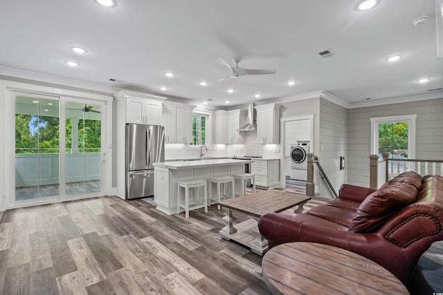 living room featuring light hardwood / wood-style floors, washer / dryer, ornamental molding, sink, and ceiling fan