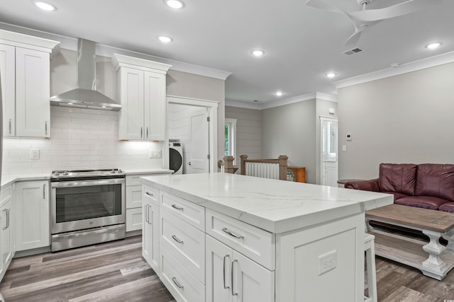 kitchen with stainless steel electric stove, wall chimney exhaust hood, wood-type flooring, crown molding, and white cabinets