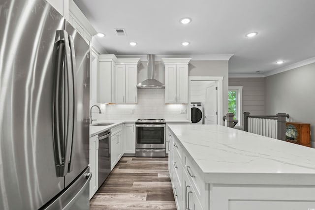 kitchen featuring ornamental molding, white cabinetry, a center island, appliances with stainless steel finishes, and wall chimney range hood