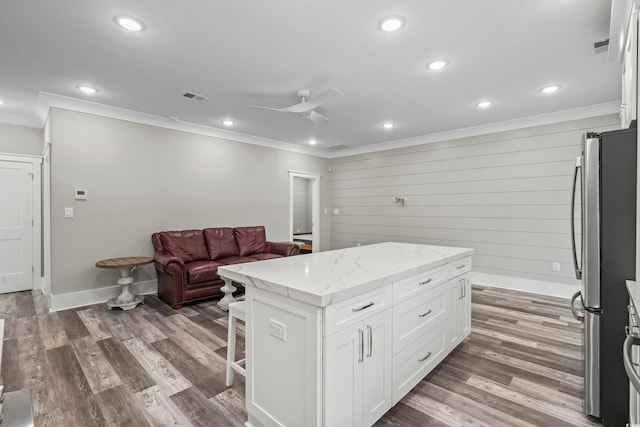 kitchen with a center island, light stone countertops, dark hardwood / wood-style flooring, white cabinetry, and stainless steel fridge