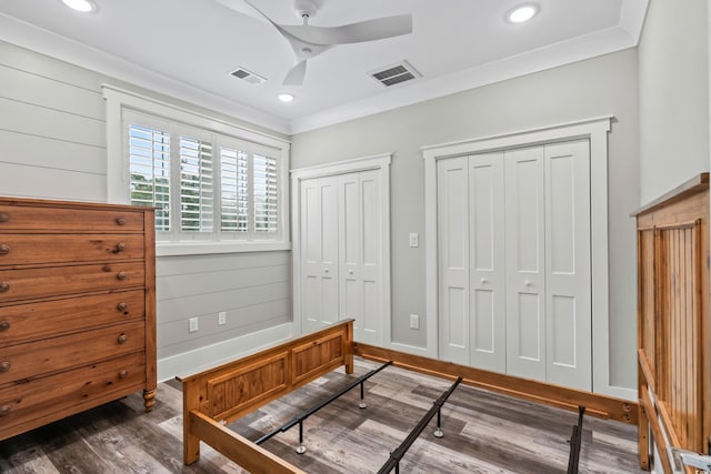 bedroom featuring dark wood-type flooring, ceiling fan, crown molding, and multiple closets