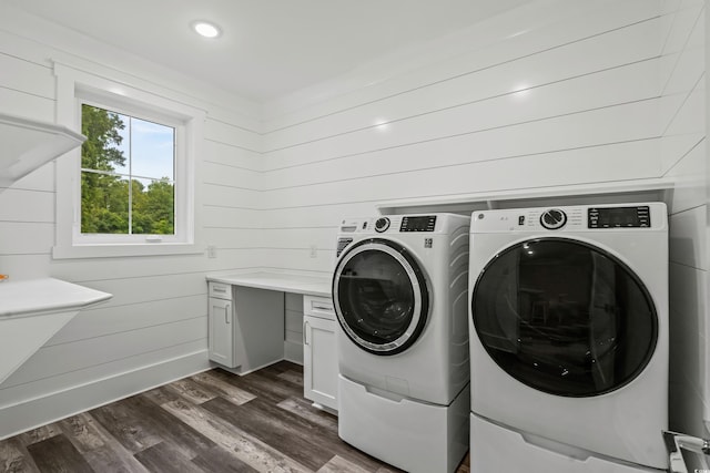 laundry room featuring dark wood-type flooring, washer and clothes dryer, wood walls, and cabinets