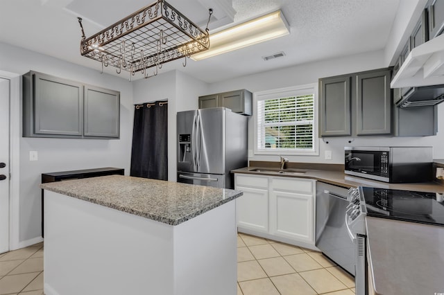 kitchen featuring light tile patterned floors, gray cabinets, stainless steel appliances, a center island, and sink