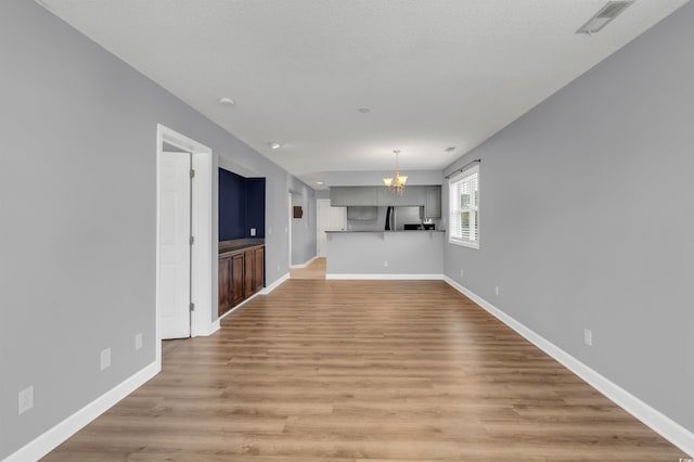 unfurnished living room with a chandelier, a textured ceiling, and hardwood / wood-style floors