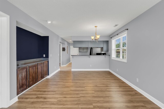 unfurnished living room with an inviting chandelier and light hardwood / wood-style flooring